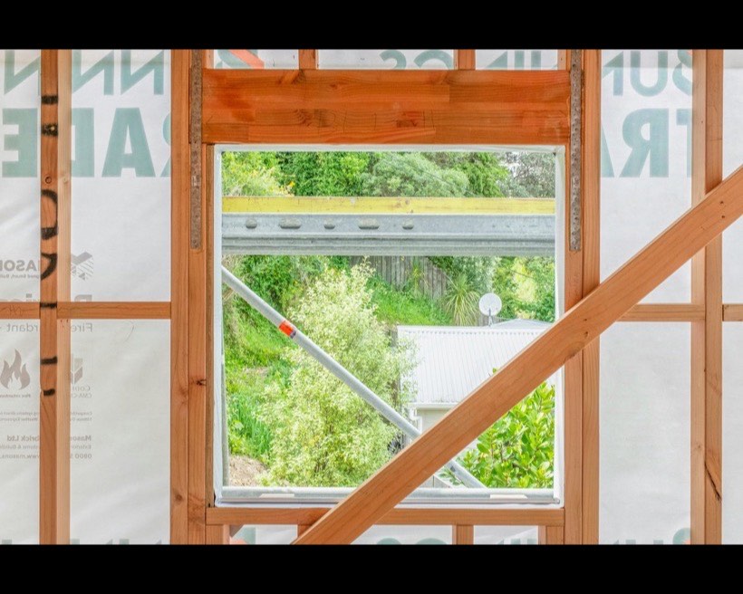 A new window opening framed in a timber stud wall, looking out to a Colorbond roof and gum trees